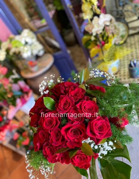 Bouquet di rose rosse confezionato con verdi selezionati.